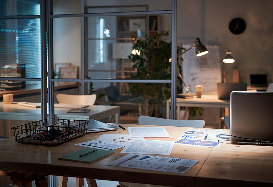 Stůl s papíry, na kterých jsou vyzobrazené grafy a analýzy, notebookem a dalšími věcmi v moderní kanceláři